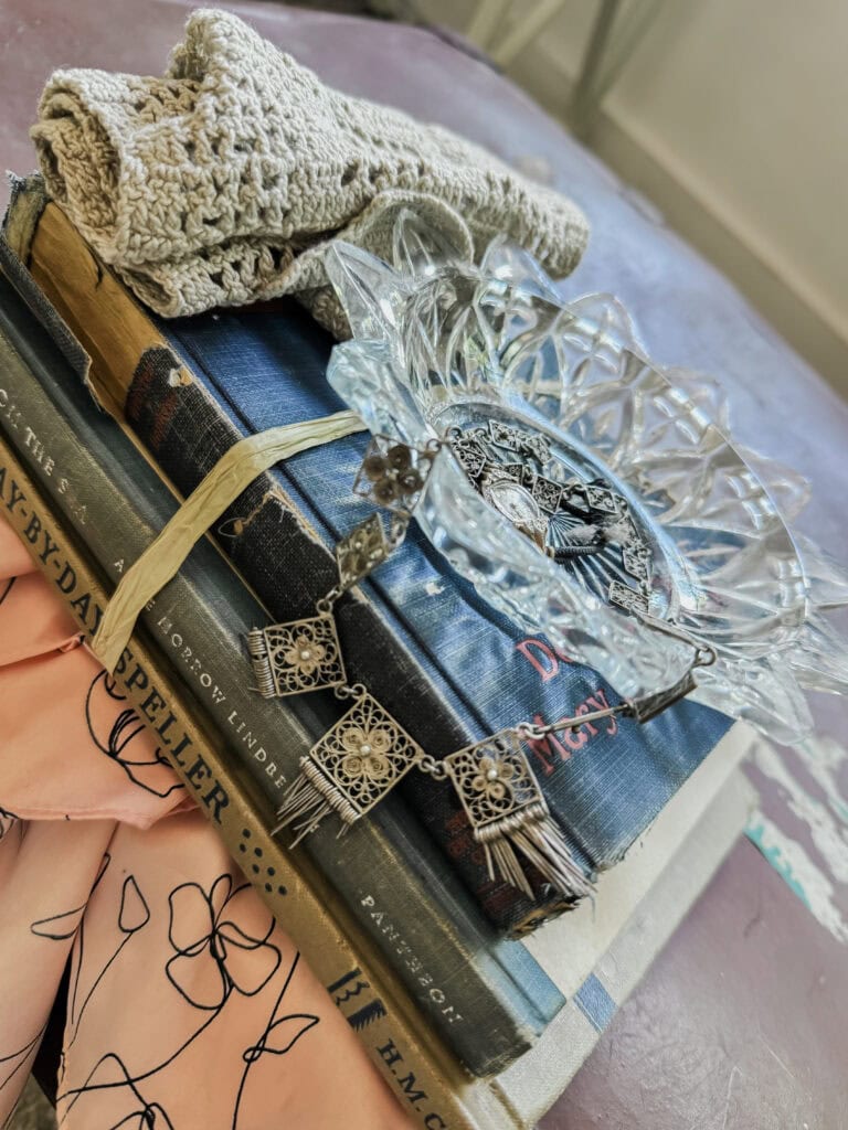 Vintage books, a glass dish, and a knitted cloth arranged on a table, creating a cozy and nostalgic aesthetic for home decor or vintage collection displays.