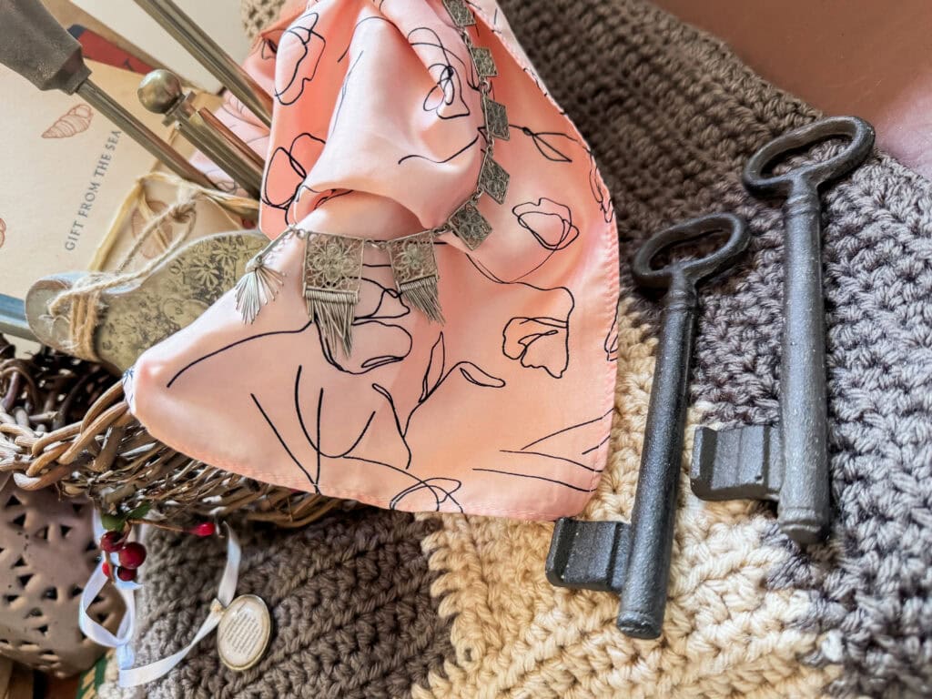 Close-up of vintage keys, a pink silk scarf with floral design, and knitted fabric, showcasing a collection of stylish and nostalgic items for home decor or fashion.