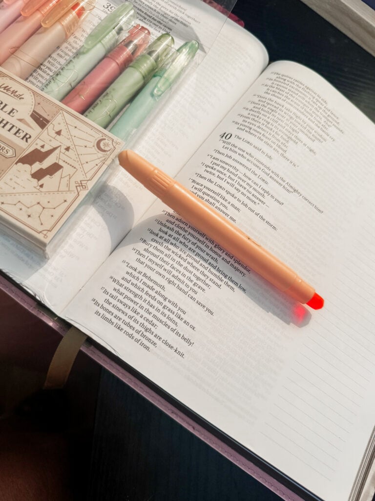 Open Bible with highlighted passages, pastel highlighters, and a red pen on a dark desk, symbolizing study and reflection for spiritual growth.