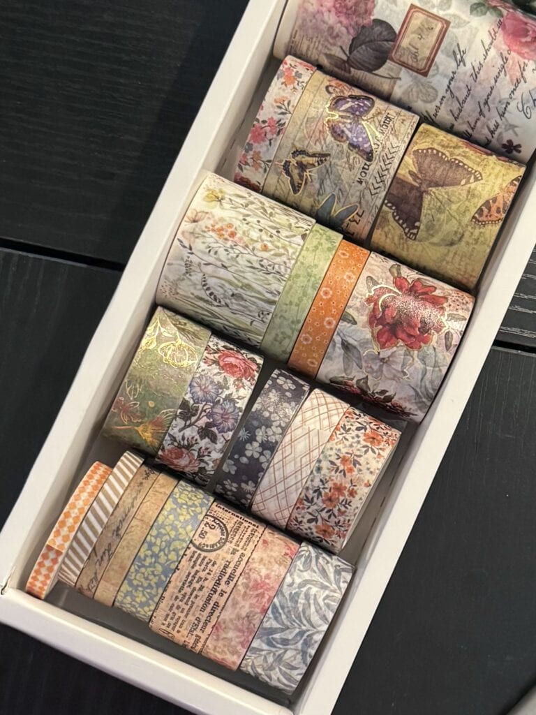 A collection of colorful and patterned washi tapes with floral, vintage, and abstract designs, neatly arranged in a white drawer for crafting and decorating.