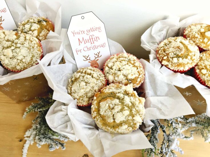 Delicious muffins with crumbly topping arranged in a gift box with a holiday tag that says "You're getting Muffin for Christmas" on a wooden surface.