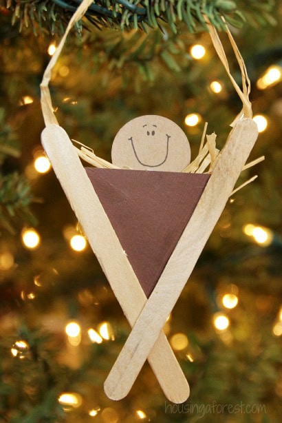Handmade Christmas tree ornament featuring a smiley face on a wooden circle, hanging from a decorated Christmas tree with warm lights in the background.