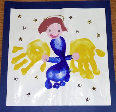 Colorful hand-painted angel drawing by a child, featuring a smiling face, blue dress, yellow wings, and surrounded by gold star stickers, on a white background with a blue border.