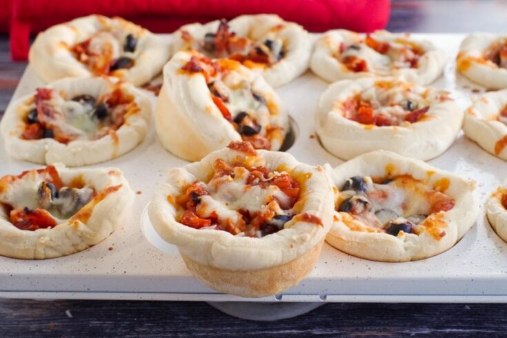 Close-up of mini pizza bites with cheese, tomato sauce, and black olives on a baking sheet, perfect for snacks or parties.