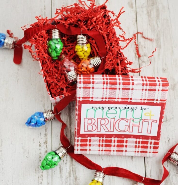 Festive Christmas gift box with colorful light bulb-shaped containers filled with candies, decorated with red shredded paper and a holiday-themed printable label.