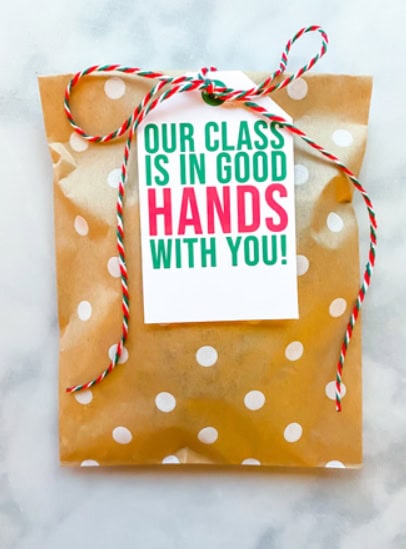 Gift bag with a note saying 'Our class is in good hands with you!' for teacher appreciation, decorated with red and white twine and polka dot paper, perfect for Christmas teacher gifts.