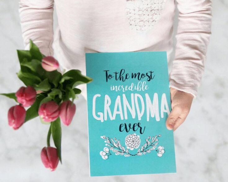 Person holding a blue Christmas card with the message 'To the most incredible Grandma ever' and a floral design, celebrating holiday gift-giving for grandma.