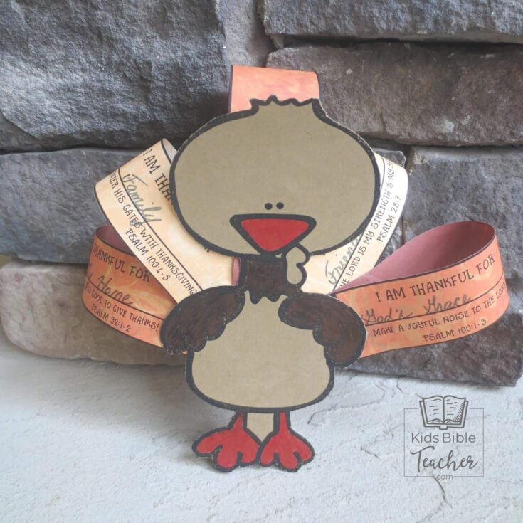 Cute paper craft of a thankful cartoon character with orange and beige paper ribbons, placed against a stone wall background, for kids' Bible activities.