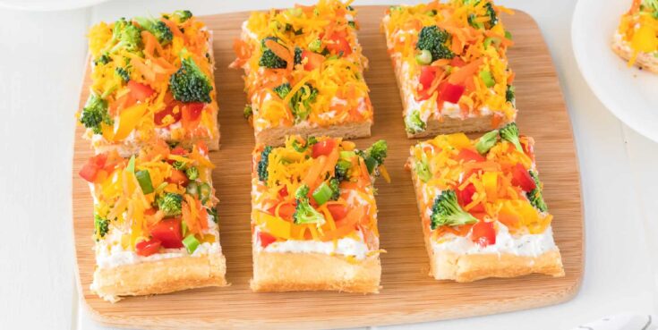 Assorted vegetable sushi bites topped with shredded cheese, chopped vegetables, and herbs on a wooden serving board, perfect for healthy snacking or appetizers.