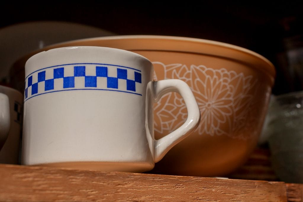 A cozy kitchen setting featuring a vintage mug and decorative bowl set on a wooden shelf.