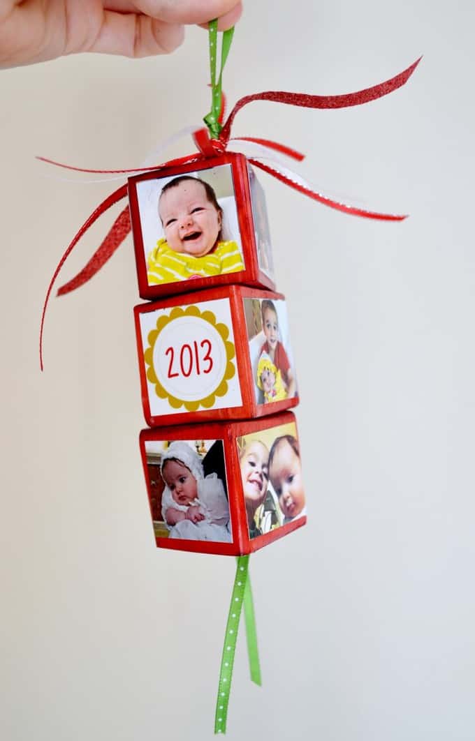 Colorful photo cube ornament with four pictures of a smiling baby, a toddler, and a child, decorated with red and green ribbons, celebrating 2013, perfect for family keepsakes.