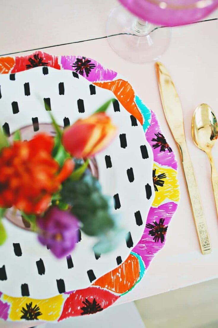 Vibrant table setting featuring a black and white polka dot plate, a colorful floral border, a gold spoon, and a blurred floral centerpiece with orange, purple, and pink flowers.