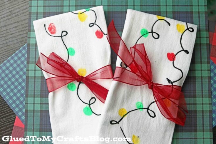 Two white cloth napkins decorated with colorful string lights and tied with red ribbons, perfect for holiday table settings and celebrations.