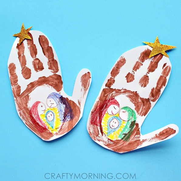 Two paper handprints decorated as baby Jesus with colorful drawings and gold star embellishments, representing a Christmas craft project for children.