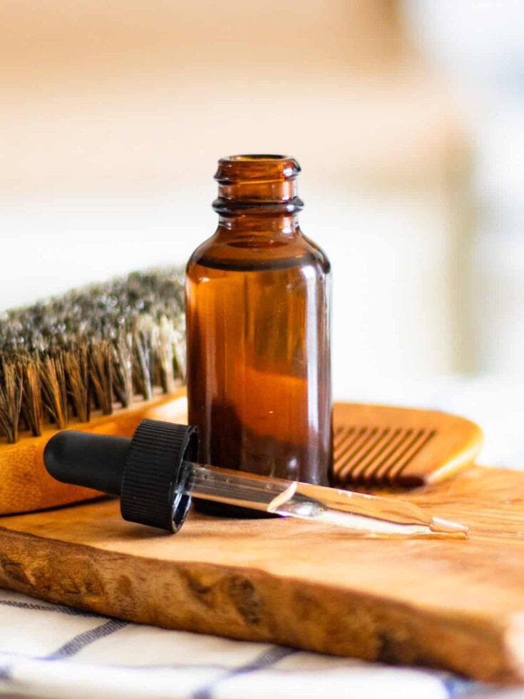Amber glass dropper bottle with essential oil, wooden comb, and brush on a rustic wooden board, ideal for aromatherapy and natural wellness.