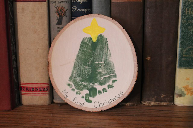 Wooden Christmas tree ornament with a yellow star and the words "My first Christmas" on a bookshelf with vintage books.