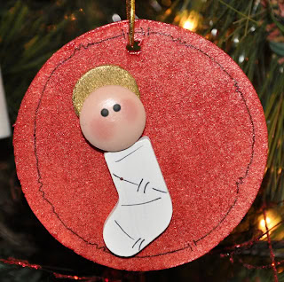 Decorative Christmas ornament featuring a cute baby Jesus figure with a golden halo, hanging on a Christmas tree branch, celebrating the holiday season.