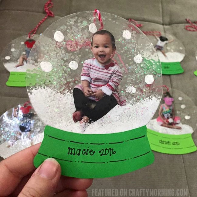 Child inside a snow globe with a green base labeled 'macee 2016', surrounded by other similar snow globes, capturing a joyful moment for a keepsake or gift.
