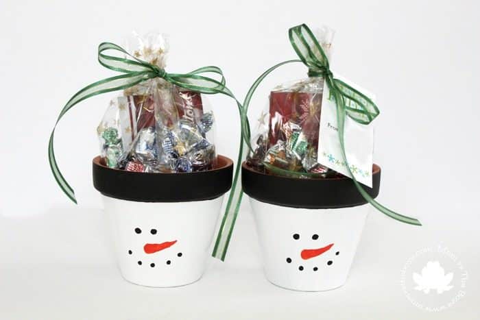 Two snowman-themed gift cups filled with assorted candies, decorated with green ribbons and a cheerful snowman face, perfect for holiday treats and Christmas celebrations.