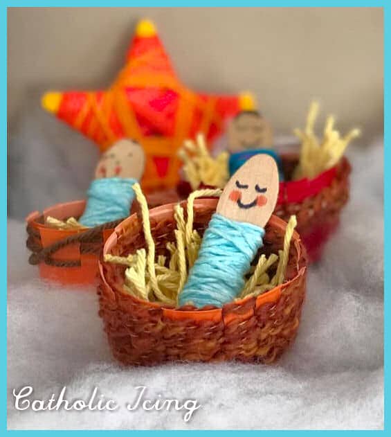 Handmade Catholic-themed Christmas craft with smiling finger puppets in small woven baskets and a colorful star decoration in the background.