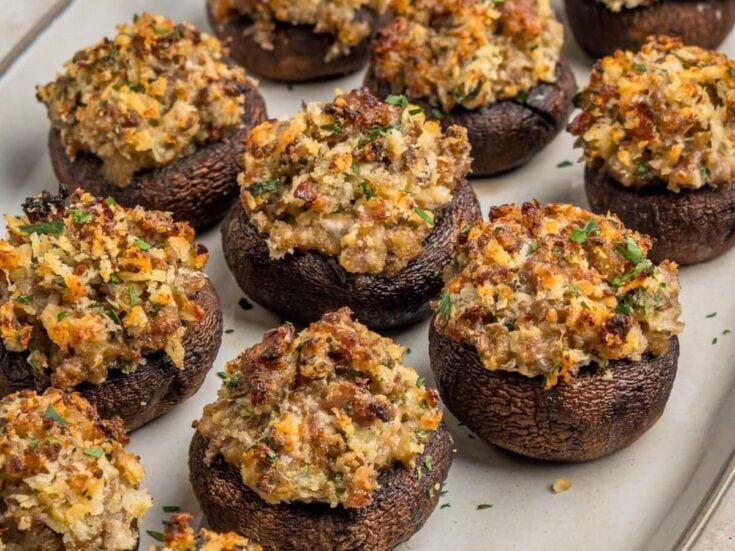 Close-up of baked stuffed mushrooms with breadcrumb topping, garnished with herbs, on a baking sheet, showcasing a savory appetizer for gatherings.