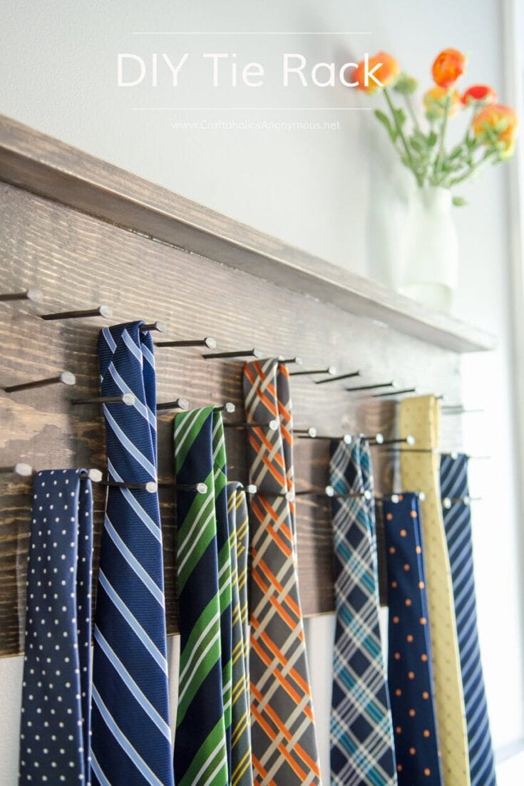 Colorful ties hanging on a DIY tie rack mounted on a wooden wall, with a vase of orange flowers in the background, showcasing a creative organization solution.