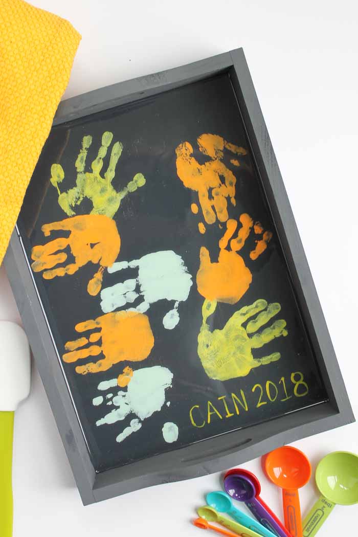 Colorful handprints in orange, green, and white on a black background, framed in a gray box, representing children's artwork for CAIN 2018.