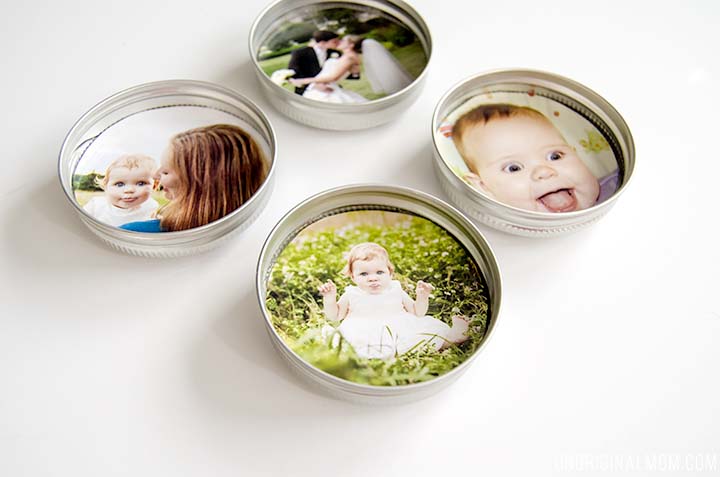 Four tin cans with baby photos, including a baby girl with a bow, a baby with a tongue out, a baby with a woman, and a baby sitting outdoors in nature.