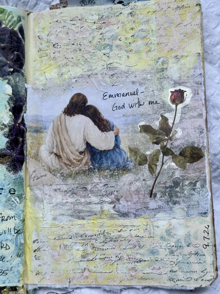A watercolor painting of two women sitting together, one with long brown hair and the other with short hair, with a rose plant nearby, and the words 'Emmanuel - God with me' written on the page.