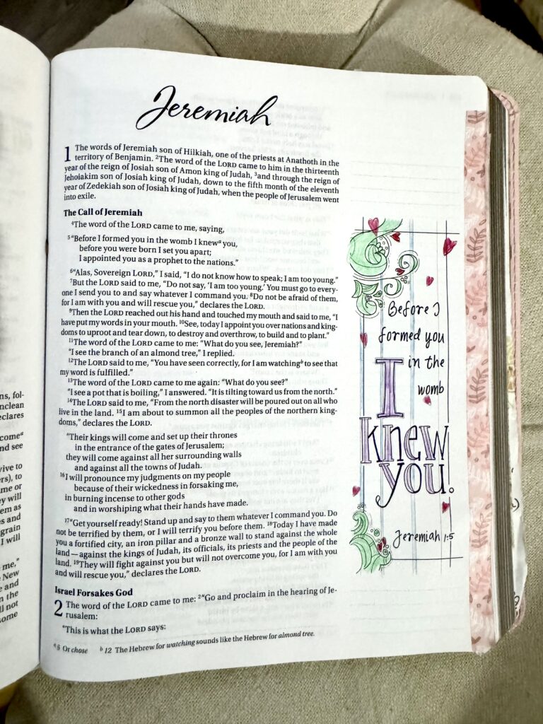 Colorful hand-drawn illustration of Jeremiah 1:5 with a scroll, flowers, and decorative elements, emphasizing the biblical message about God's knowledge before birth.