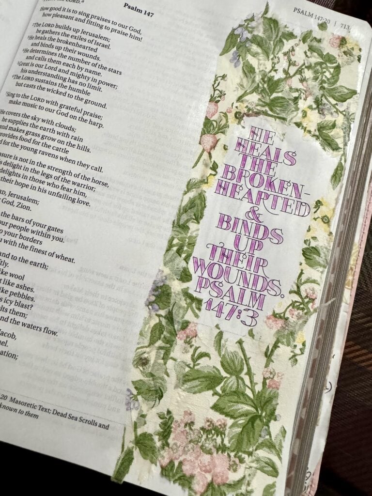 Bible page with a floral border and the verse 'He heals the brokenhearted and binds up their wounds' from Psalm 147:3, emphasizing healing and faith.