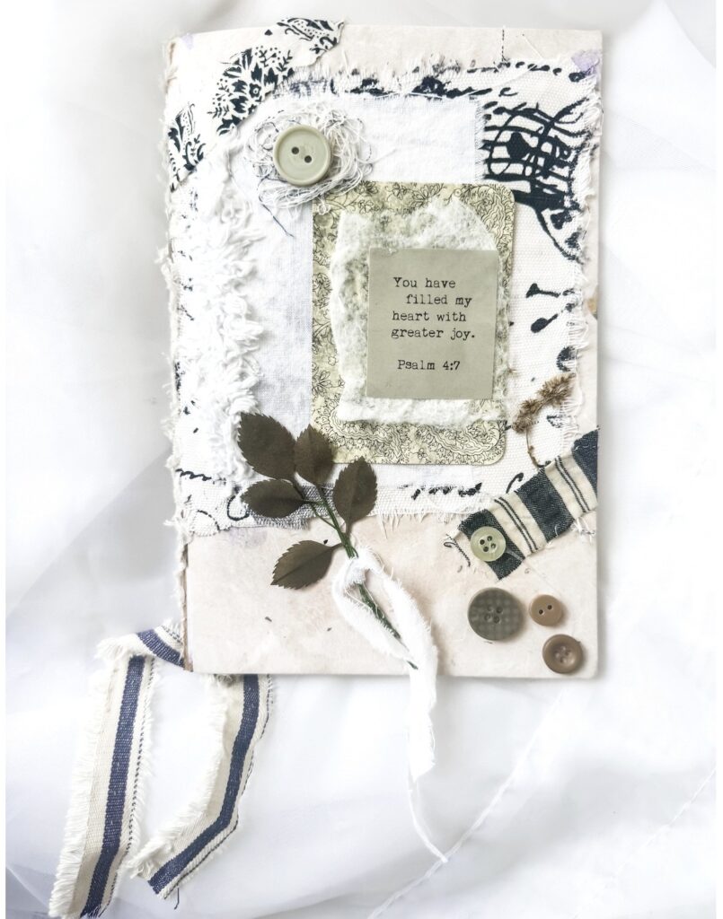 Handmade journal cover with fabric, buttons, a Bible verse, and decorative elements, symbolizing faith and joy, perfect for spiritual reflection and inspiration.