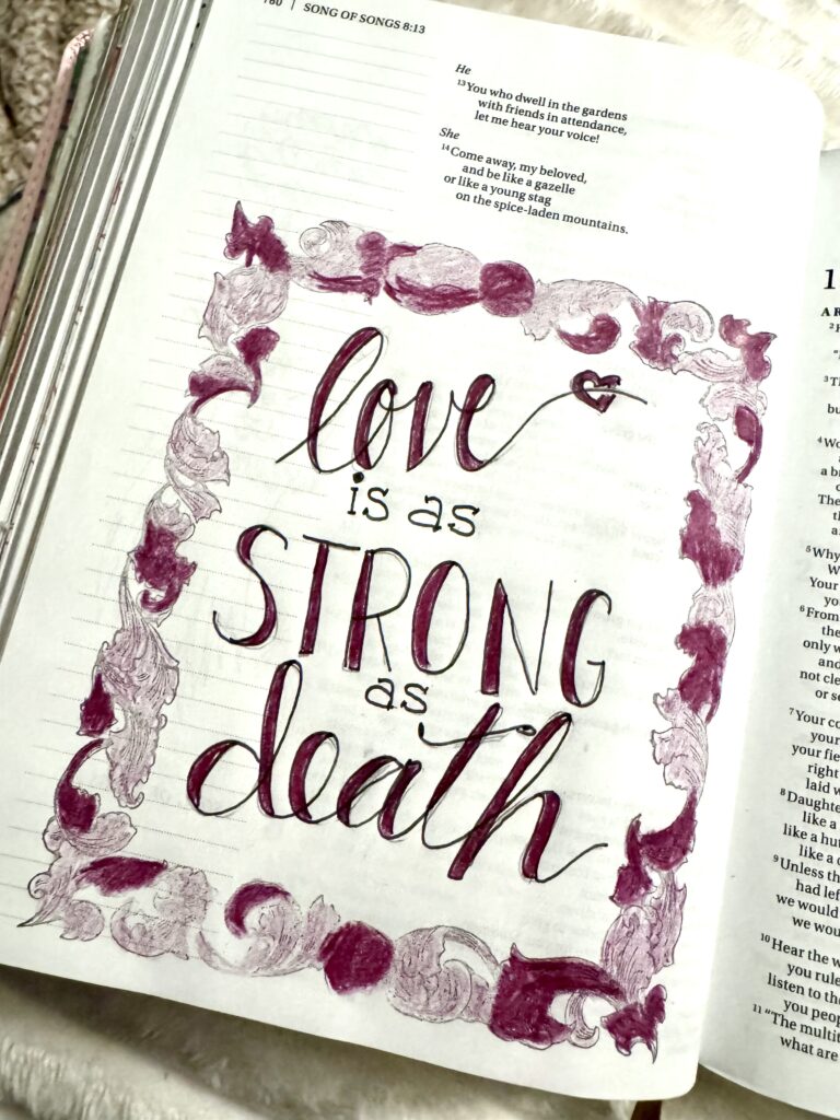 Handwritten inspirational quote in a decorated notebook page, surrounded by pink and purple watercolor floral border, emphasizing love and strength.