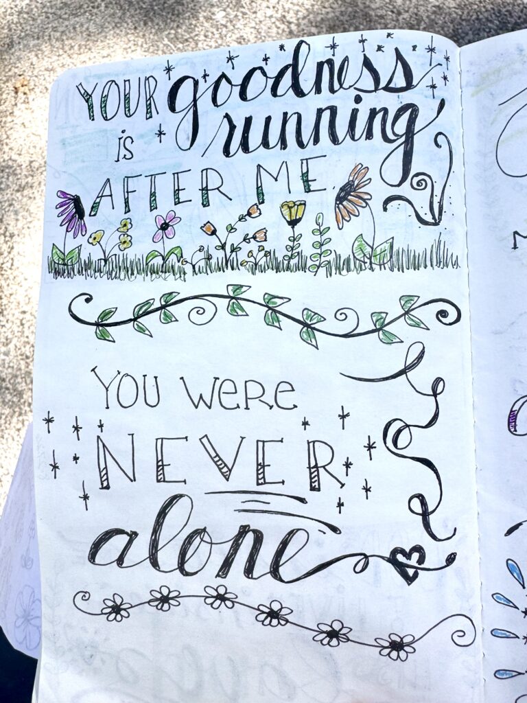 Hand drawn quote saying 'Your goodness is running after me. You were never alone' with decorative flowers and swirls, perfect for motivational or faith-based content.