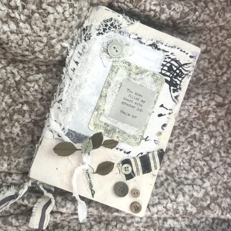 A beautifully decorated Bible journaling notebook featuring a quote, buttons, and a small branch with leaves, perfect for creative faith journaling.