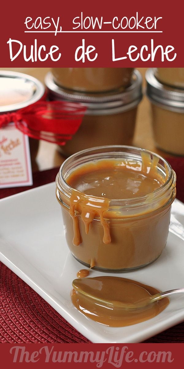 A glass jar of creamy dulce de leche with a spoonful drizzled on a plate, caramel sauce on the spoon, and jars in the background; image from The Yummy Life site promoting easy, slow-cooker dulce de le.
