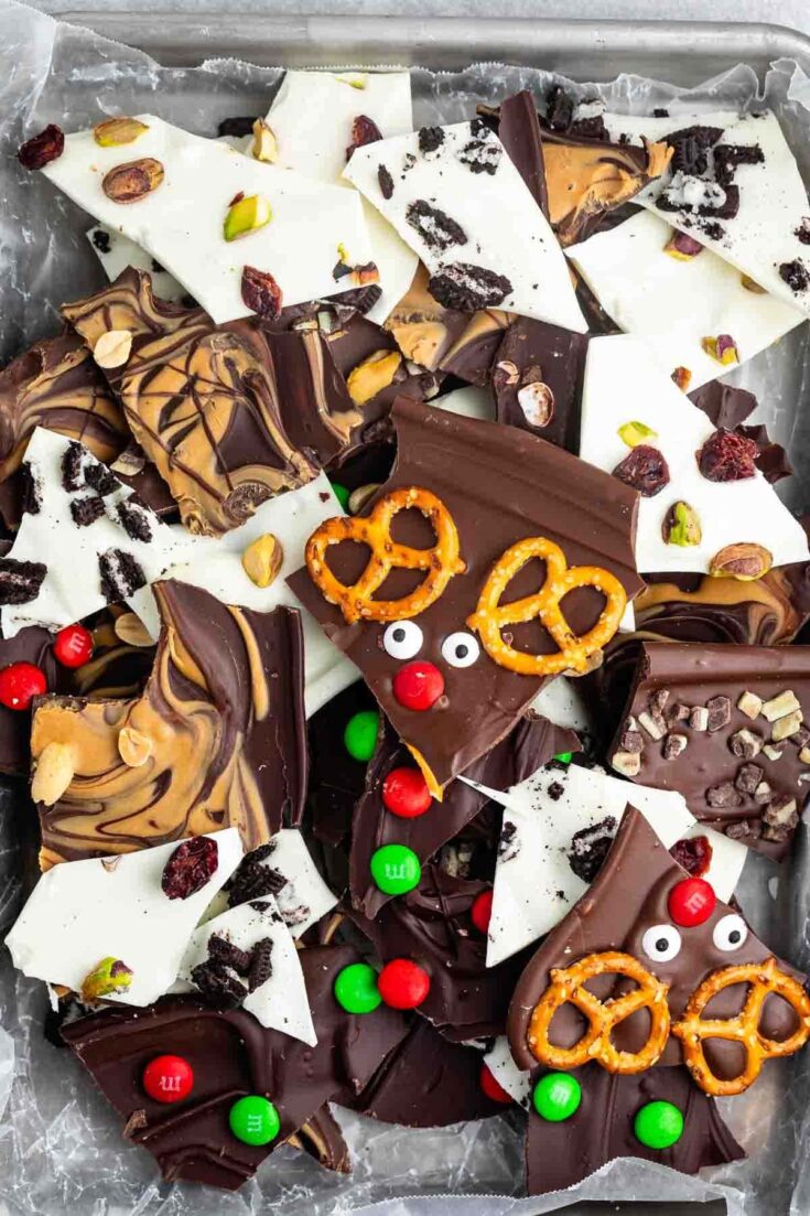 Assorted chocolate bark pieces with white and dark chocolate, pretzel twists, dried fruits, nuts, and colorful candies in a tray, styled for dessert photography.