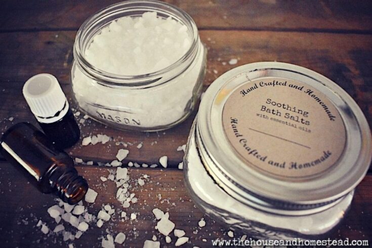 Homemade soothing bath salts in glass jars with essential oil bottle on a rustic wooden surface, featuring coarse salt crystals for a DIY spa bath experience.