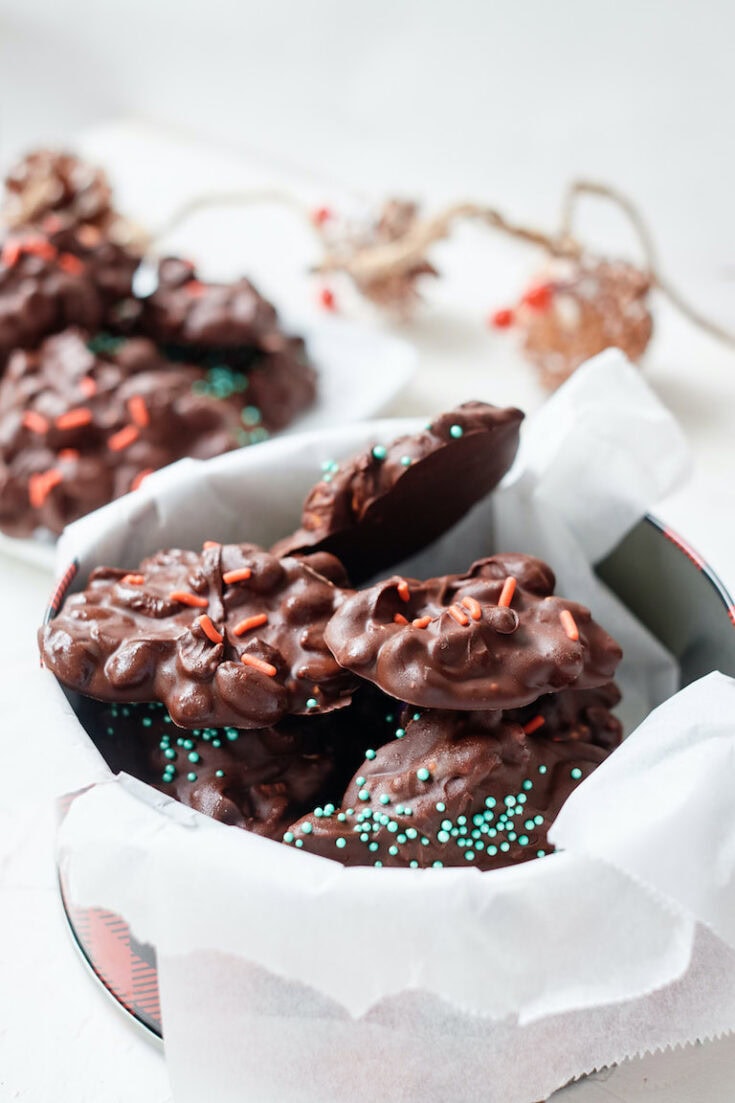 Chocolate covered cookies with mint green sprinkles in a tin, on white parchment, soft lighting, close-up for a cozy holiday dessert image.