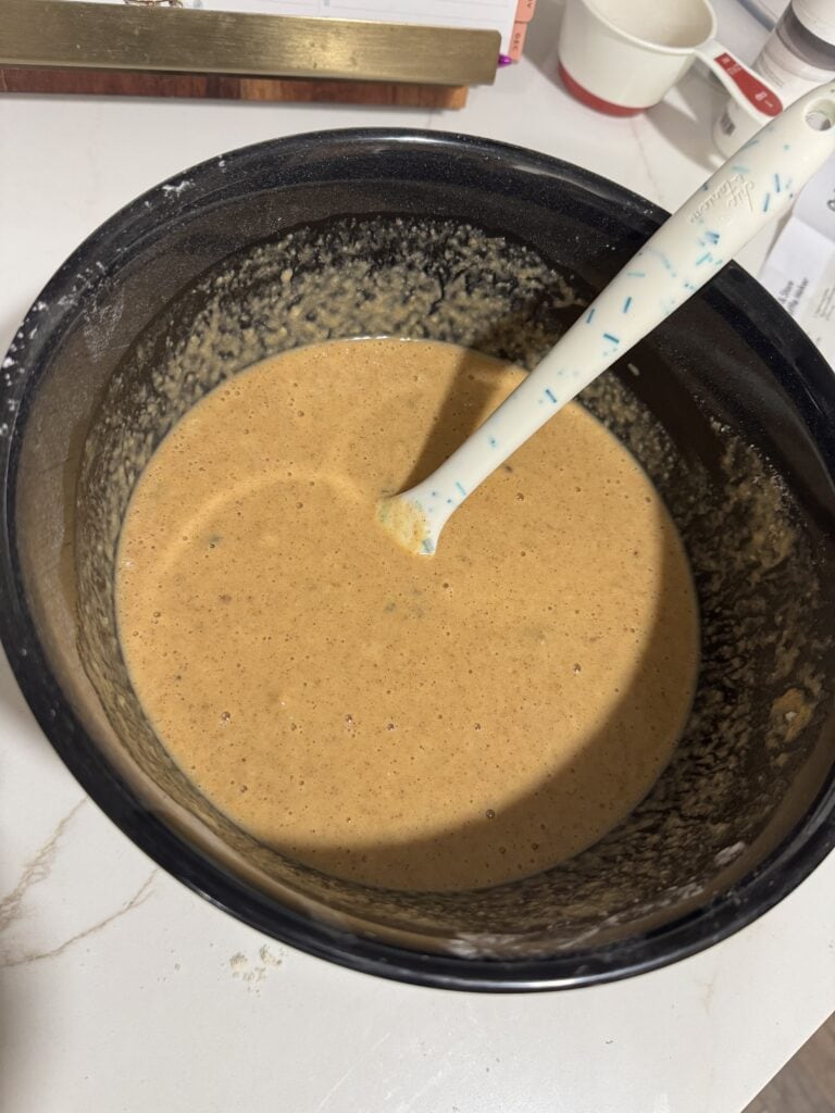 Close-up of a mixing bowl with smooth, creamy batter and a spatula inside, ready for baking or cooking, on a kitchen countertop.