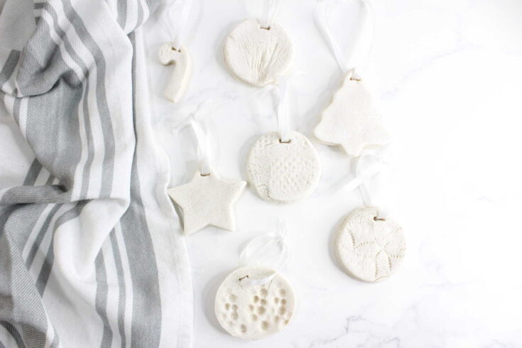White ceramic ornaments hanging on a string with a light gray striped cloth, arranged on a marble surface, capturing minimalist home decor aesthetics for A Hundred Affections.