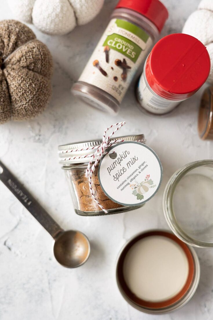 A Hundred Affections: pumpkin spice mix jar with cinnamon sticks, clove bottle, and warm beverage on marble surface, cozy kitchen scene.