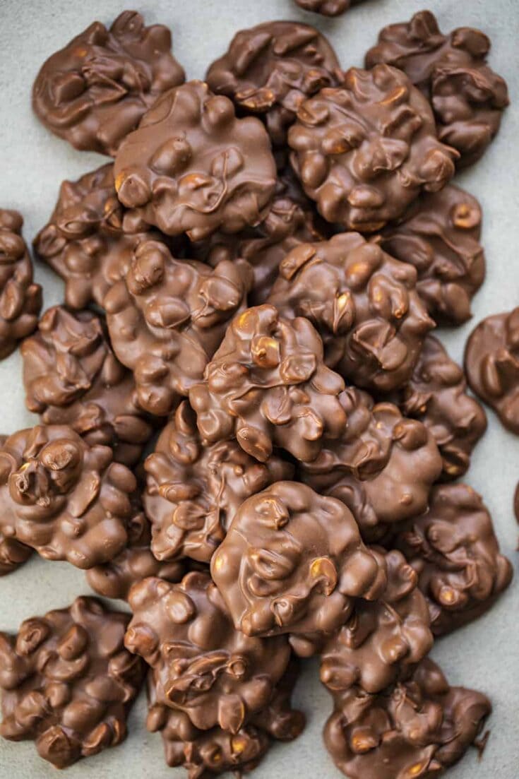 Assorted chocolate clusters with almonds and hazelnuts, glossy milk chocolate, close-up showing textured nut pieces and crisp edges.
