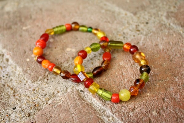 Two vibrant beaded bracelets with red, yellow, green, and brown beads, laid on a textured stone surface, showcasing handmade jewelry for women.