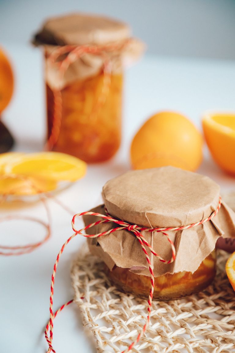 Fresh homemade orange marmalade in jars with rustic twine, set on a light surface with sliced oranges in the background.
