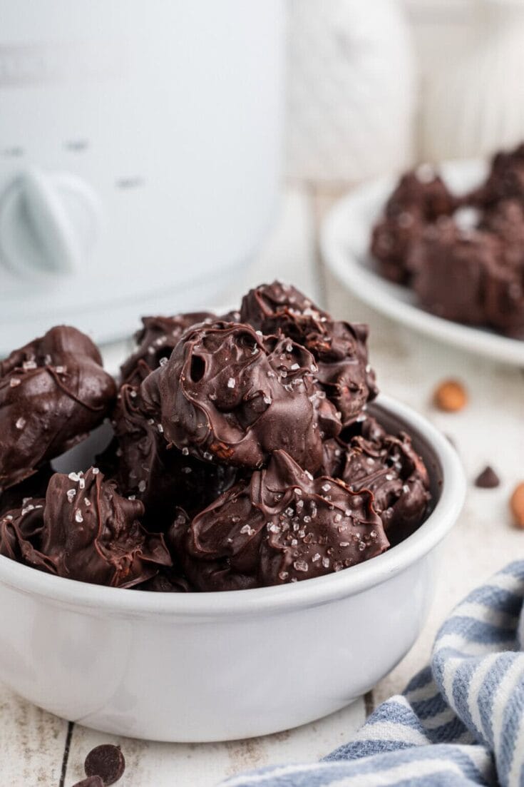 Smoky dark chocolate clusters with coarse sea salt in a white bowl on a wooden surface, close-up shot for a Hundred Affections image.