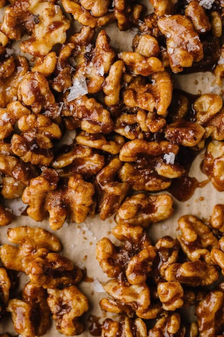 Close up of caramelized walnuts with glossy sugary coating, bar-like clusters of roasted walnuts on a neutral background, showcasing a rich autumn dessert theme.