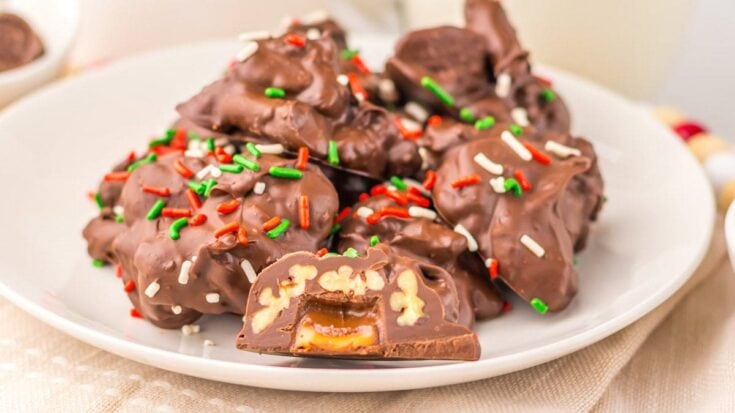 A plate of chocolate-covered candy clusters with colorful sprinkles, showcasing gooey caramel centers and a bite revealing peanut filling.
